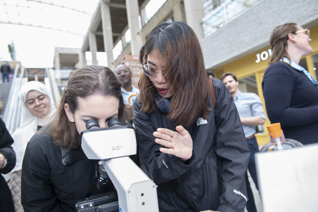 researcher with member of the public looking through microscope