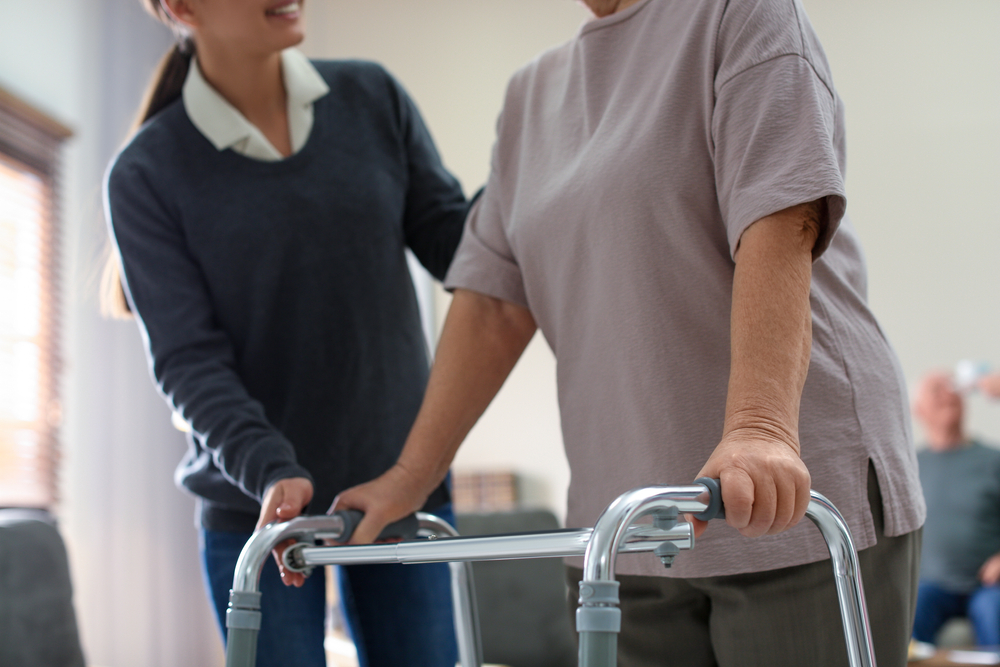 Care worker helping elderly woman using Zimmer frame to walk.