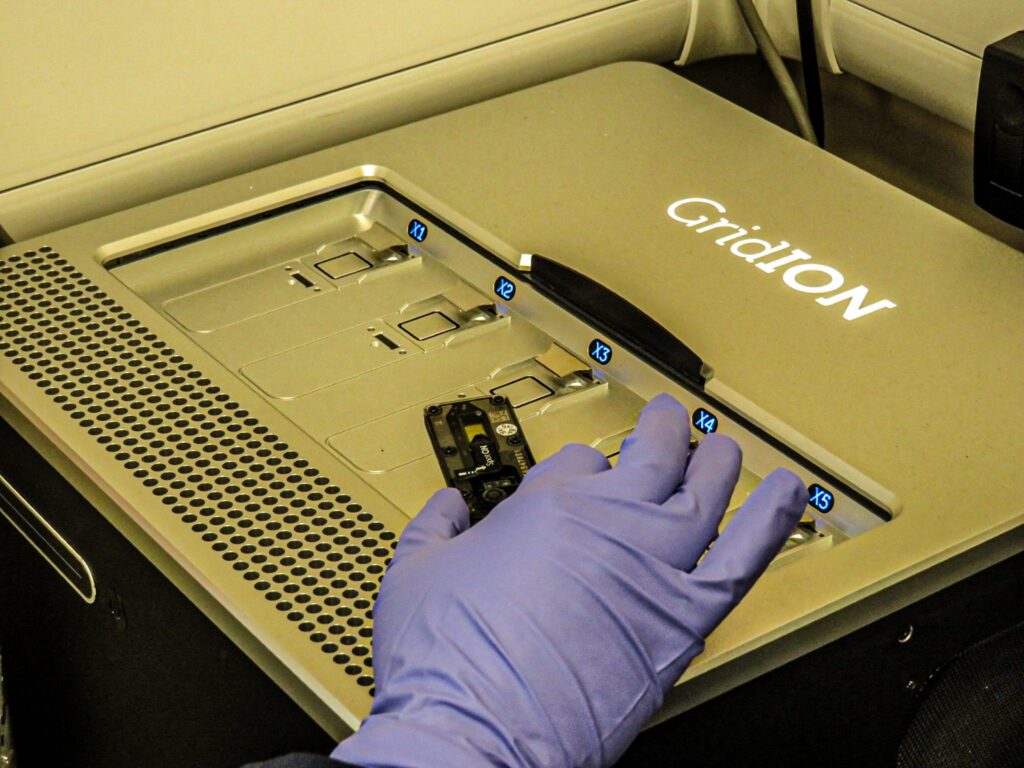 A gloved hand about to put a sample in an Oxford Nanopore Gridiron sequencing device